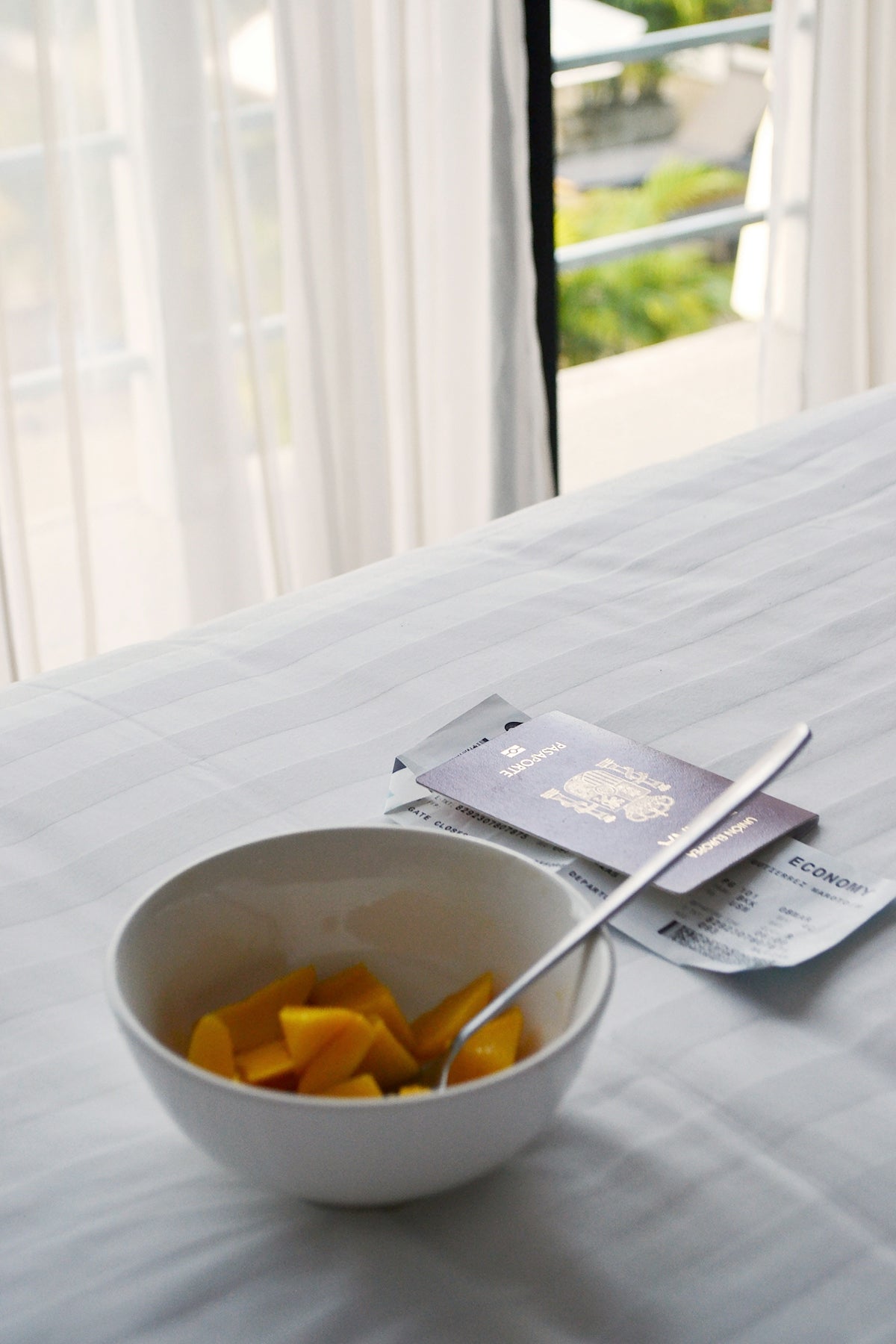 Mango bowl, passport, and plane ticket on a bed.