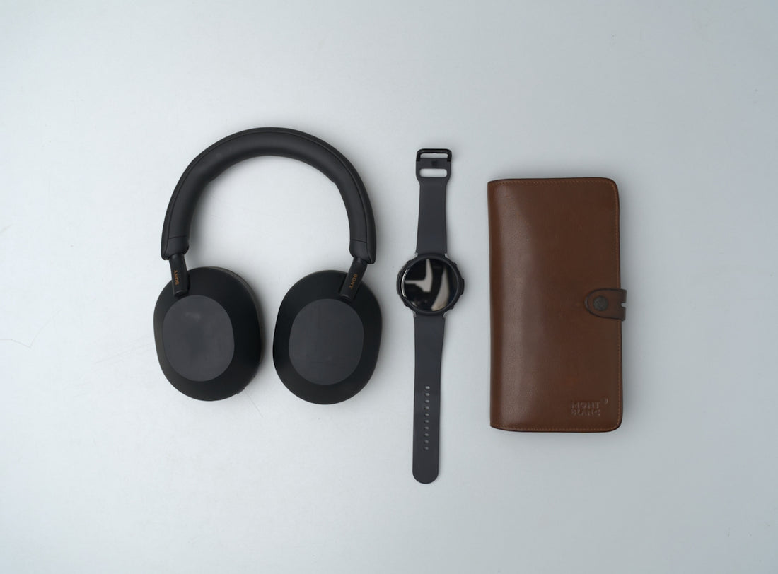 Black headphones, wristwatch, and brown wallet arranged neatly.