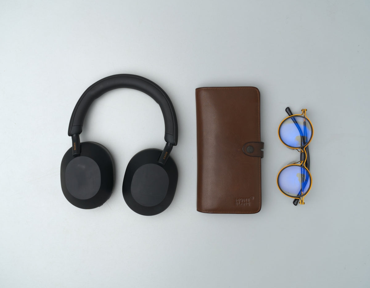 Black headphones, brown notebook, and glasses on gray background