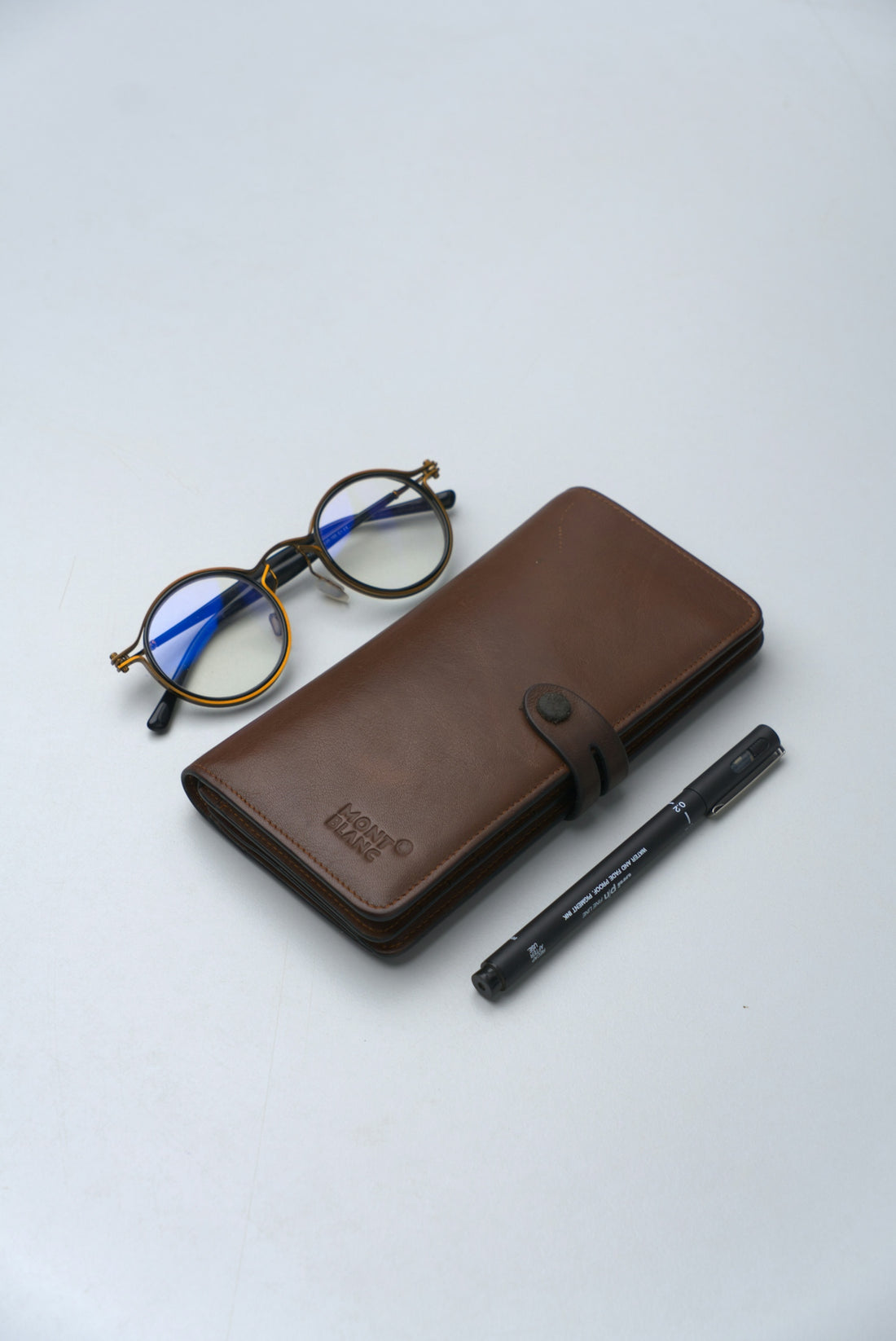 Round glasses, brown case, and pen on white surface