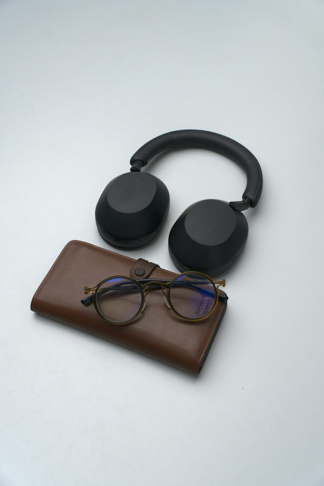 Black headphones, glasses, and brown wallet on white surface