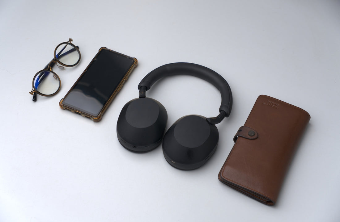 Smartphone, headphones, glasses, and wallet arranged on surface.