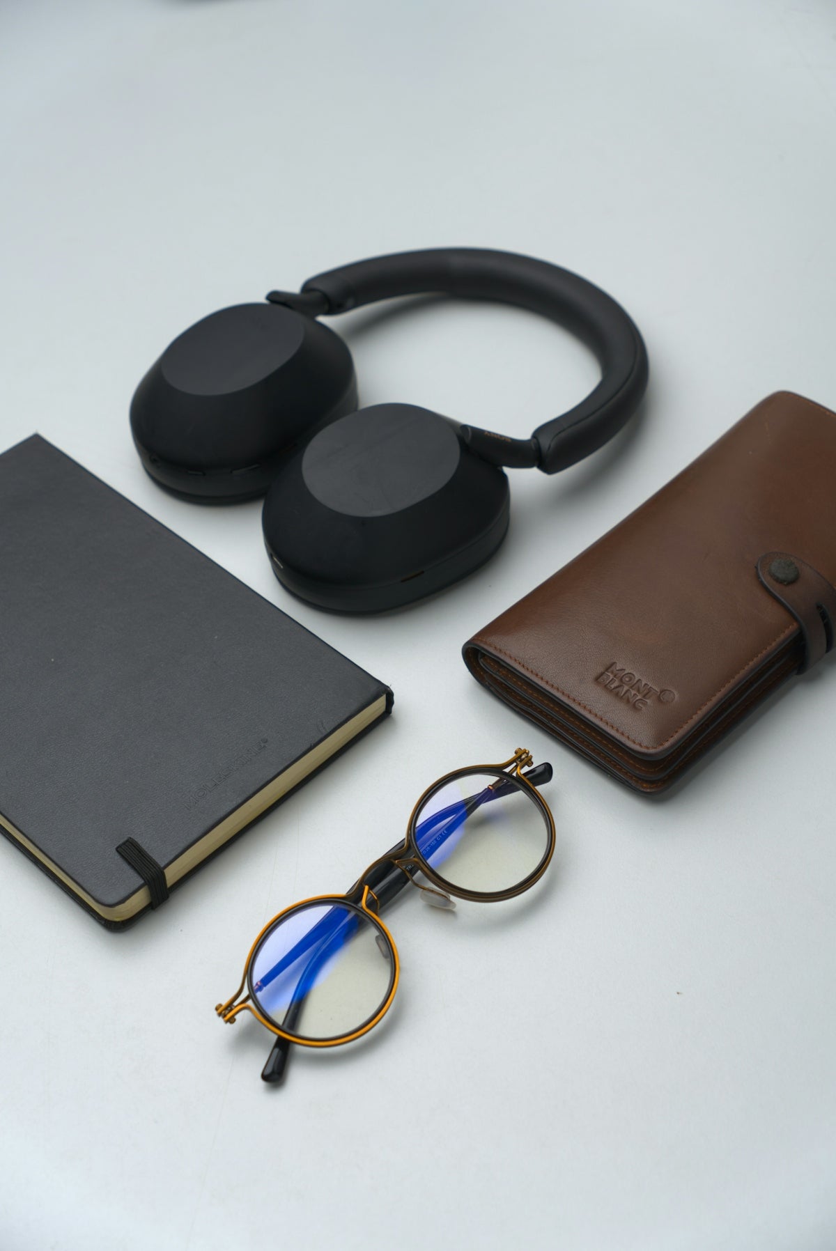 Headphones, notebook, glasses, and wallet on white surface