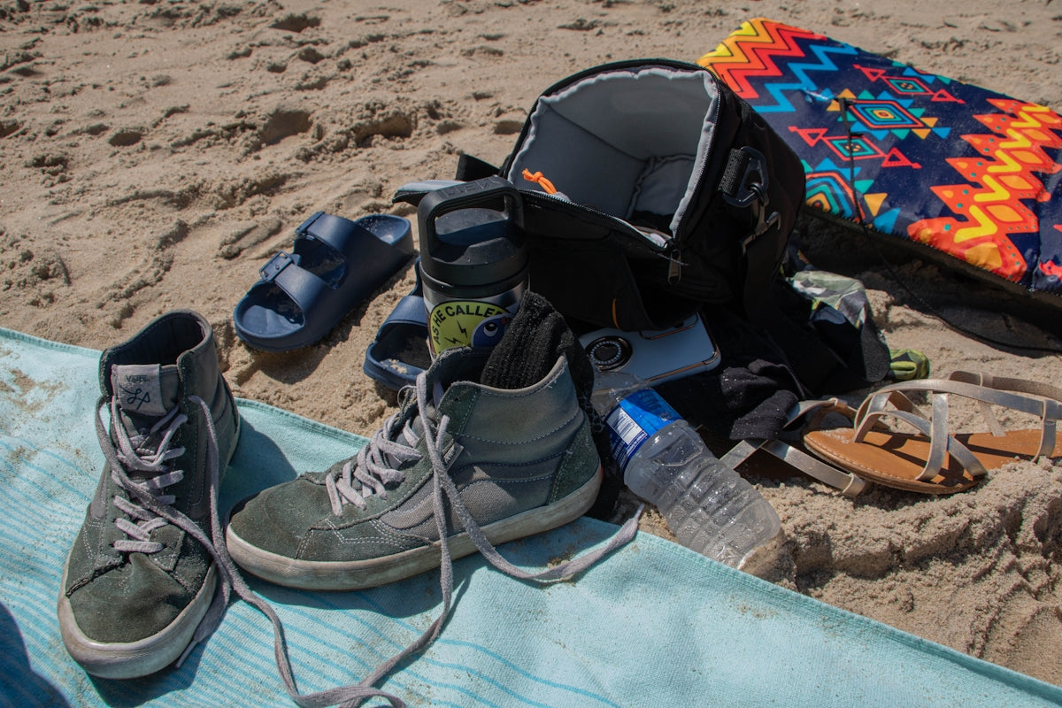 Beach gear laid out on sand with backpack and shoes.