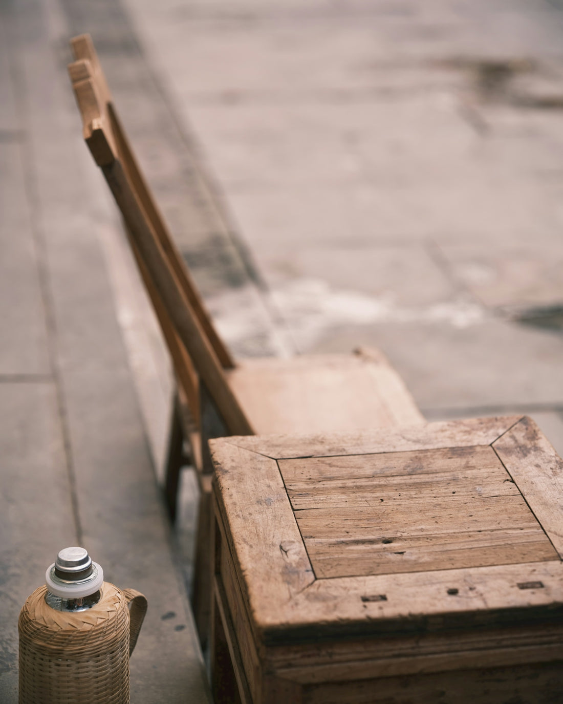 Two wooden chairs and a thermos on pavement.