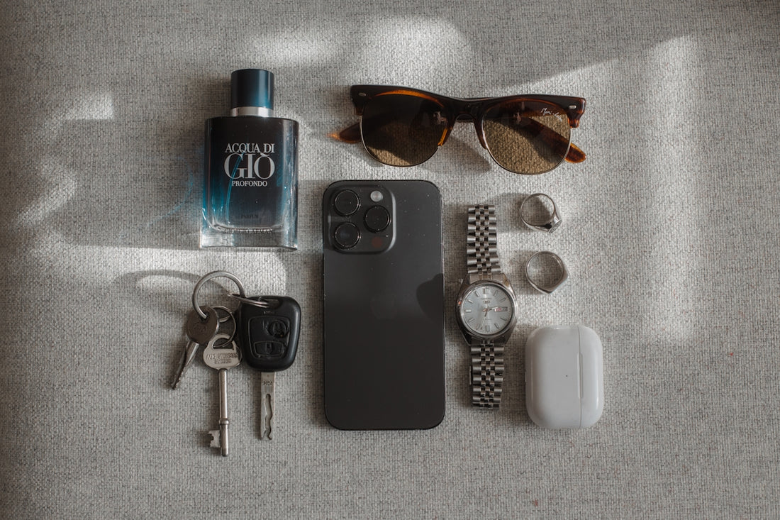 Perfume, sunglasses, phone, watch, keys, and earbuds arranged neatly arranged.
