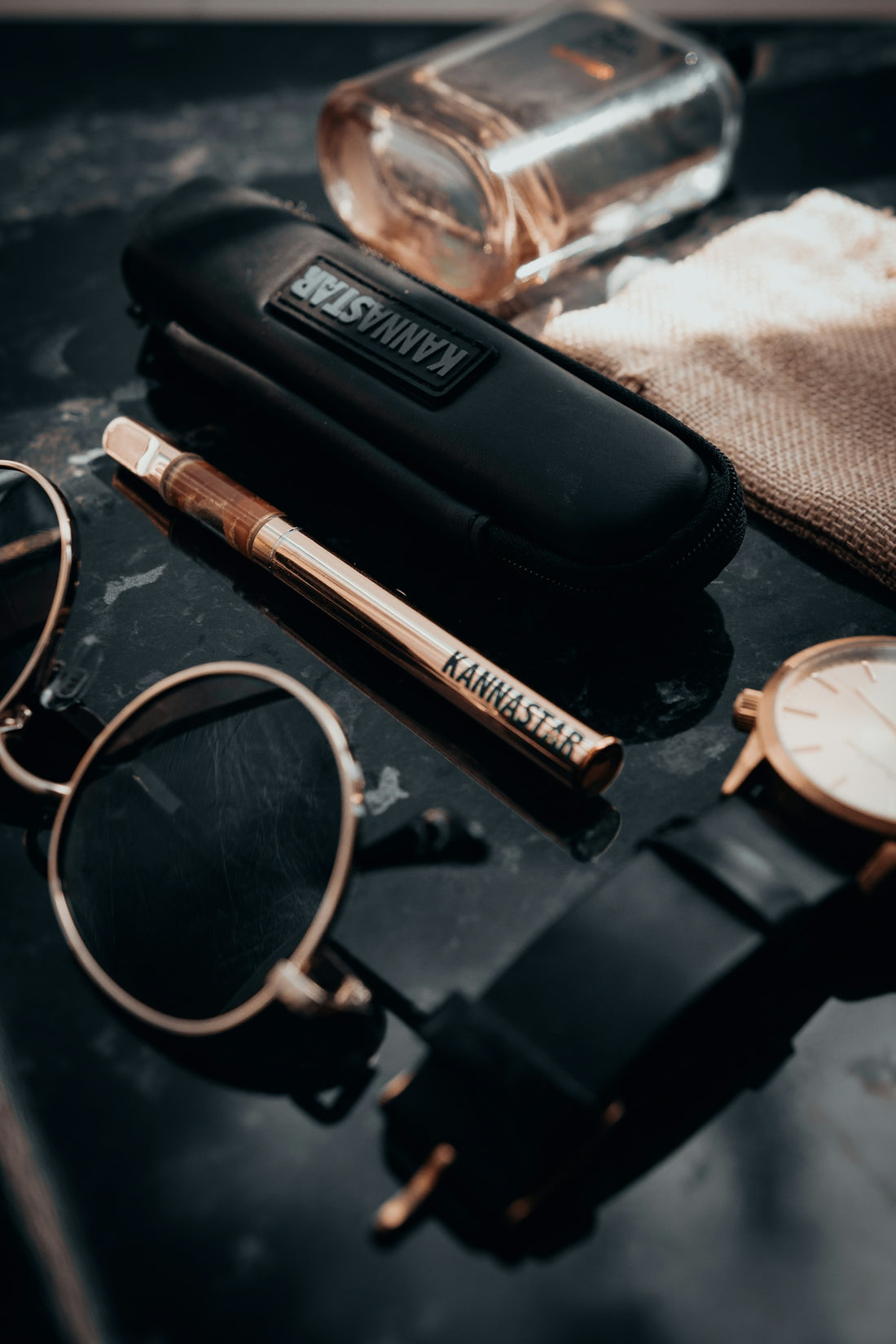 Sunglasses, vape pen, watch, and perfume bottle arranged