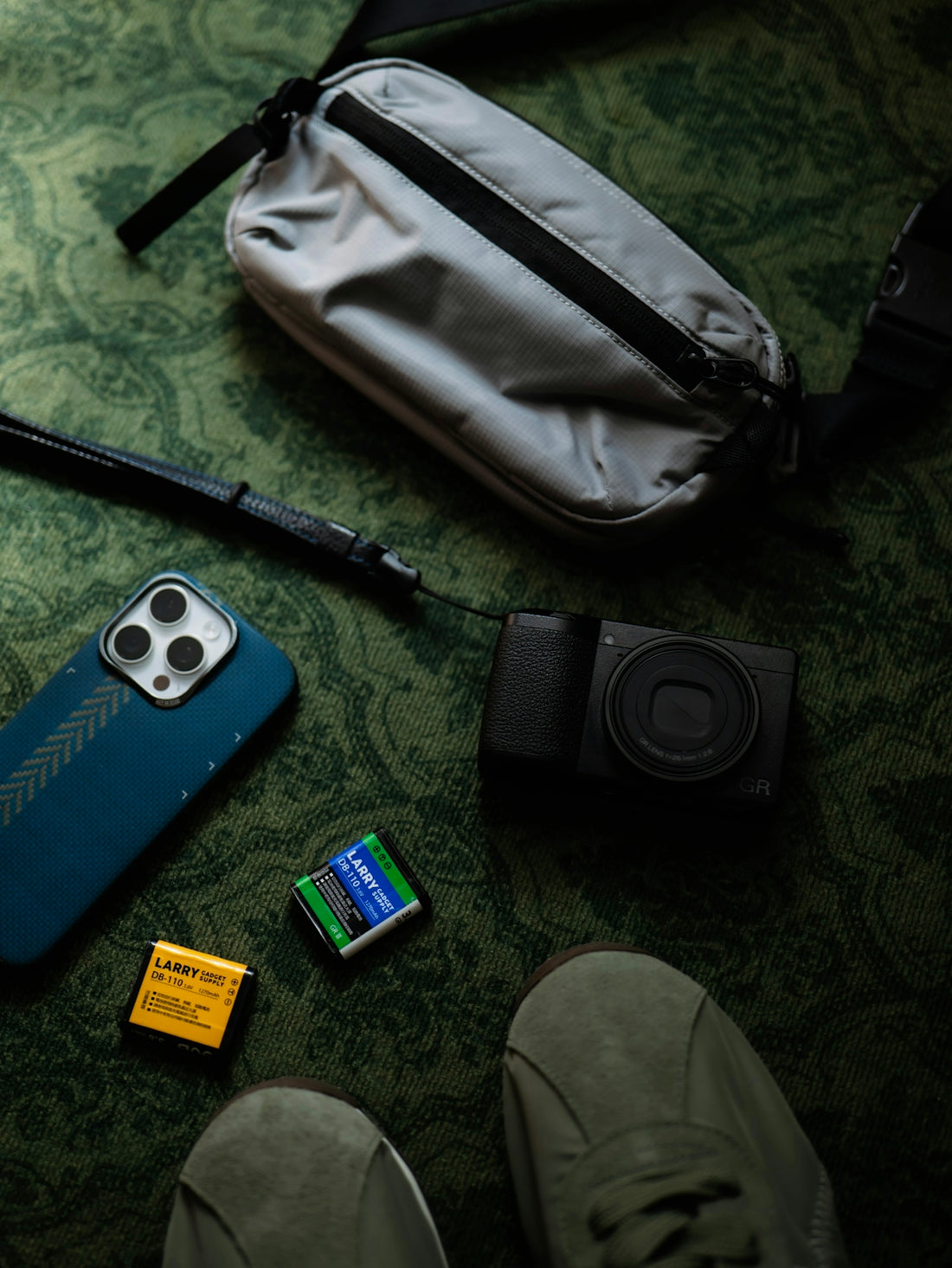 Camera, phone, film, and bag arranged on a patterned surface.