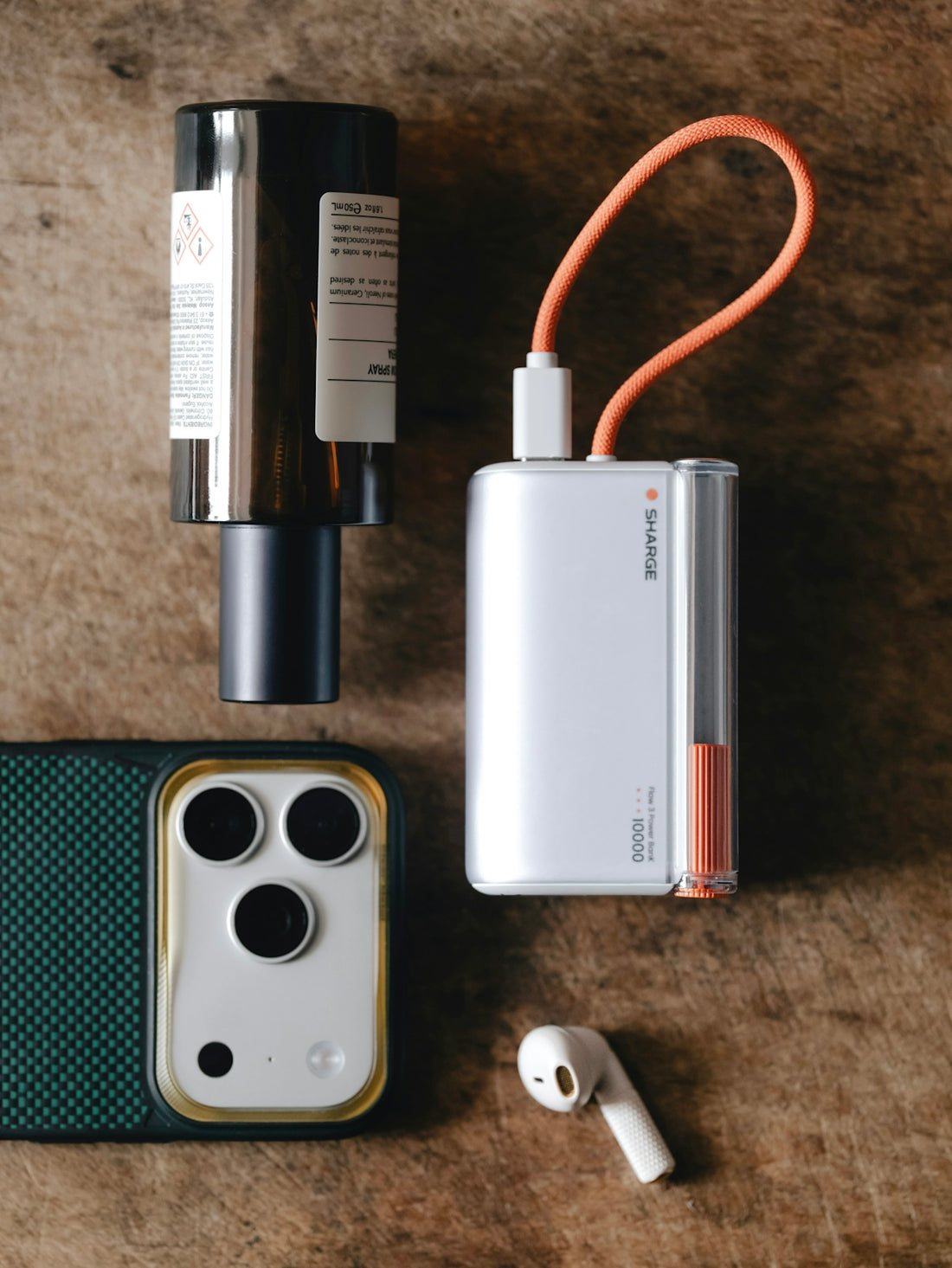 Phone, power bank, earbud, and bottle arranged on wood.