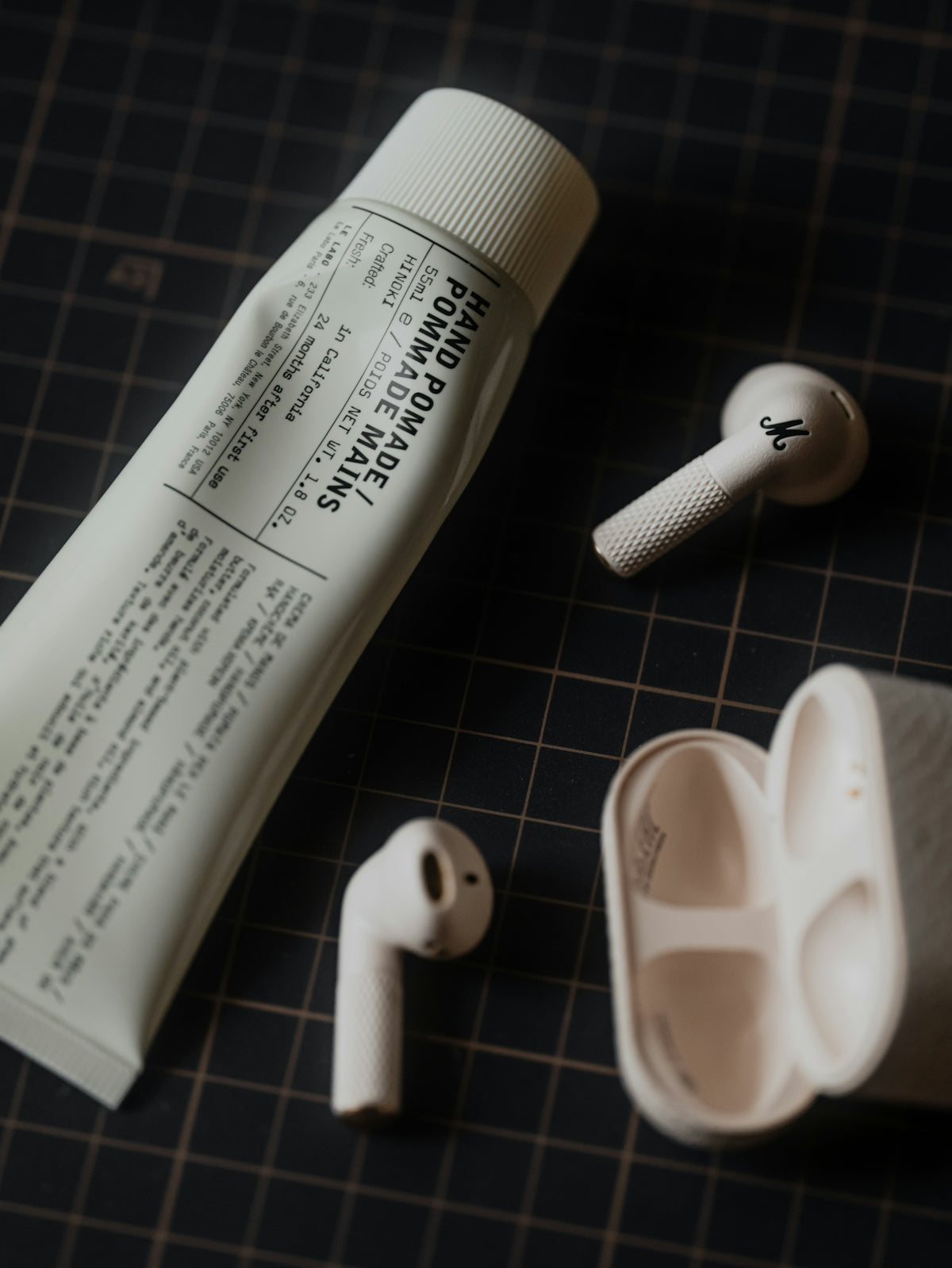 Tube of hand pomade and wireless earbuds on grid.
