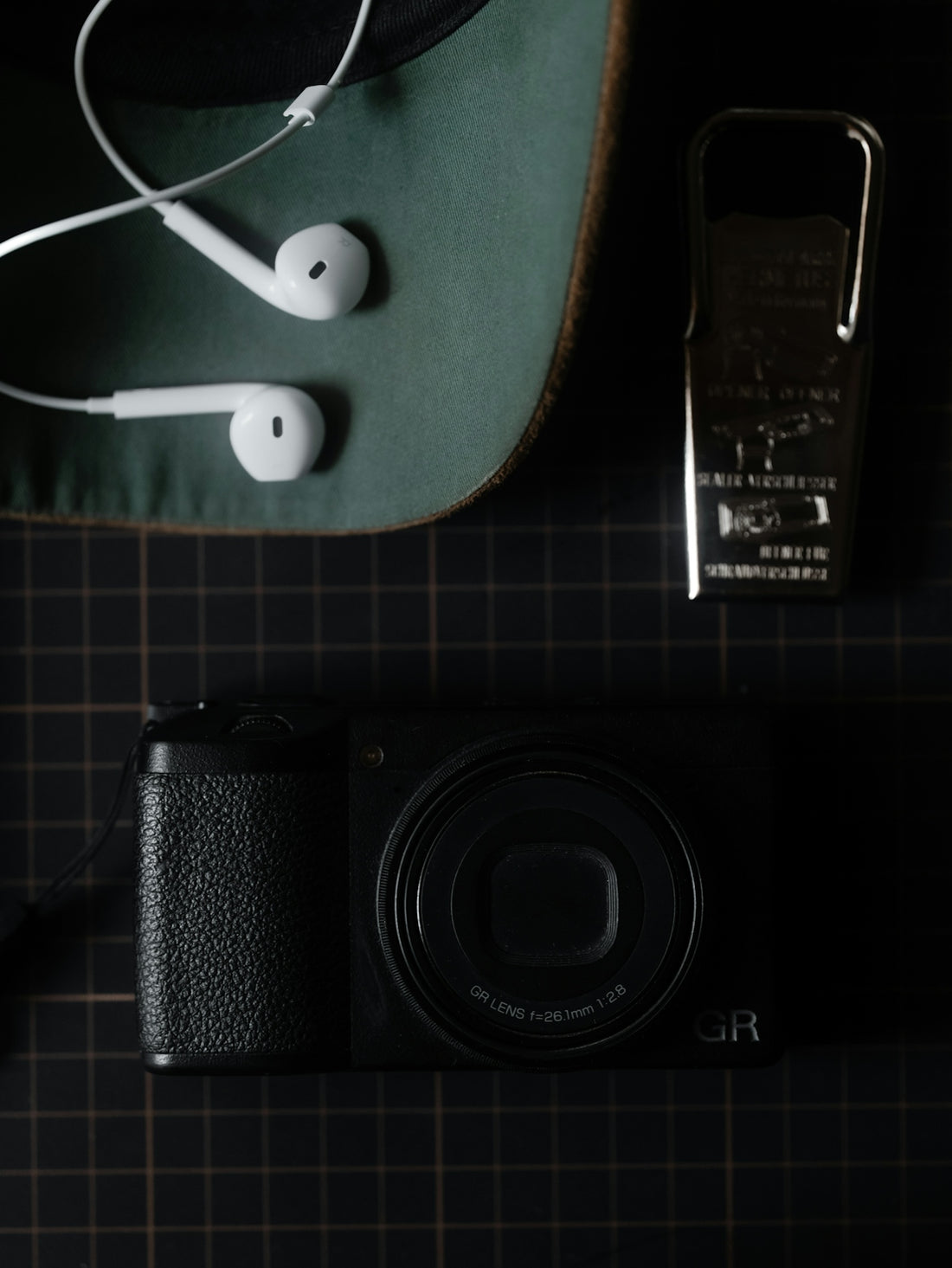 Compact camera, white earphones, and green hat on dark surface