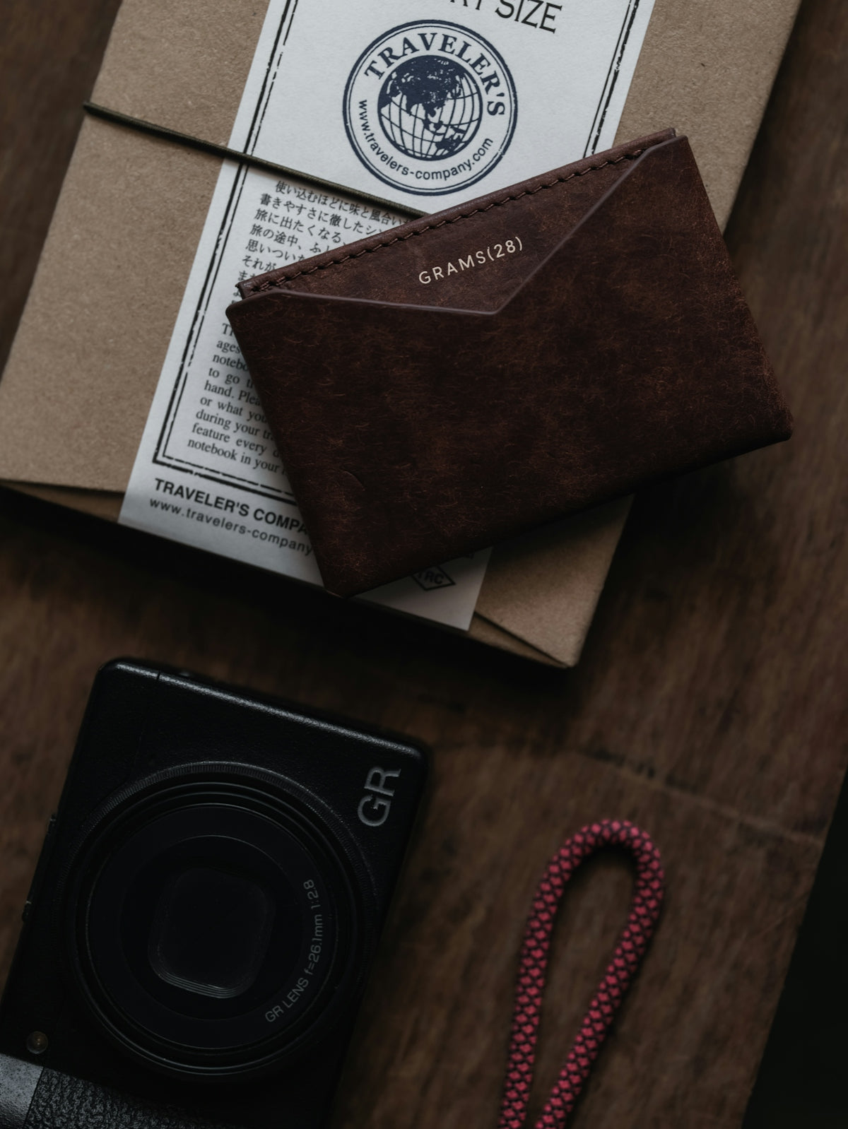 Brown leather wallet, camera, and notebook on surface