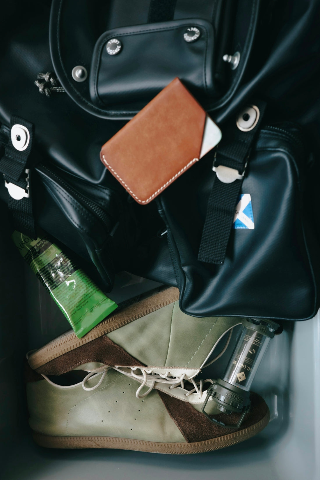 Black bag, brown wallet, green shoes, and a green tube.