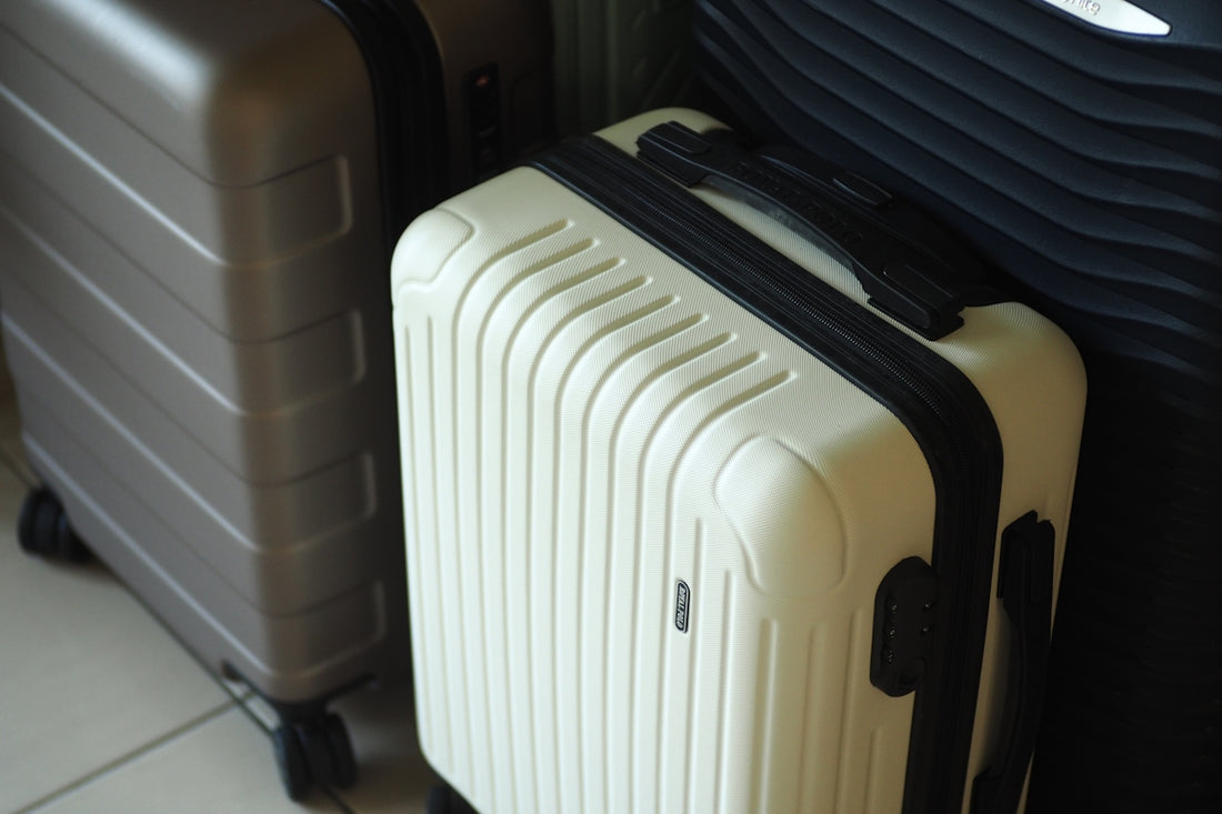 Three hard-shell suitcases in white, grey, and dark colors.