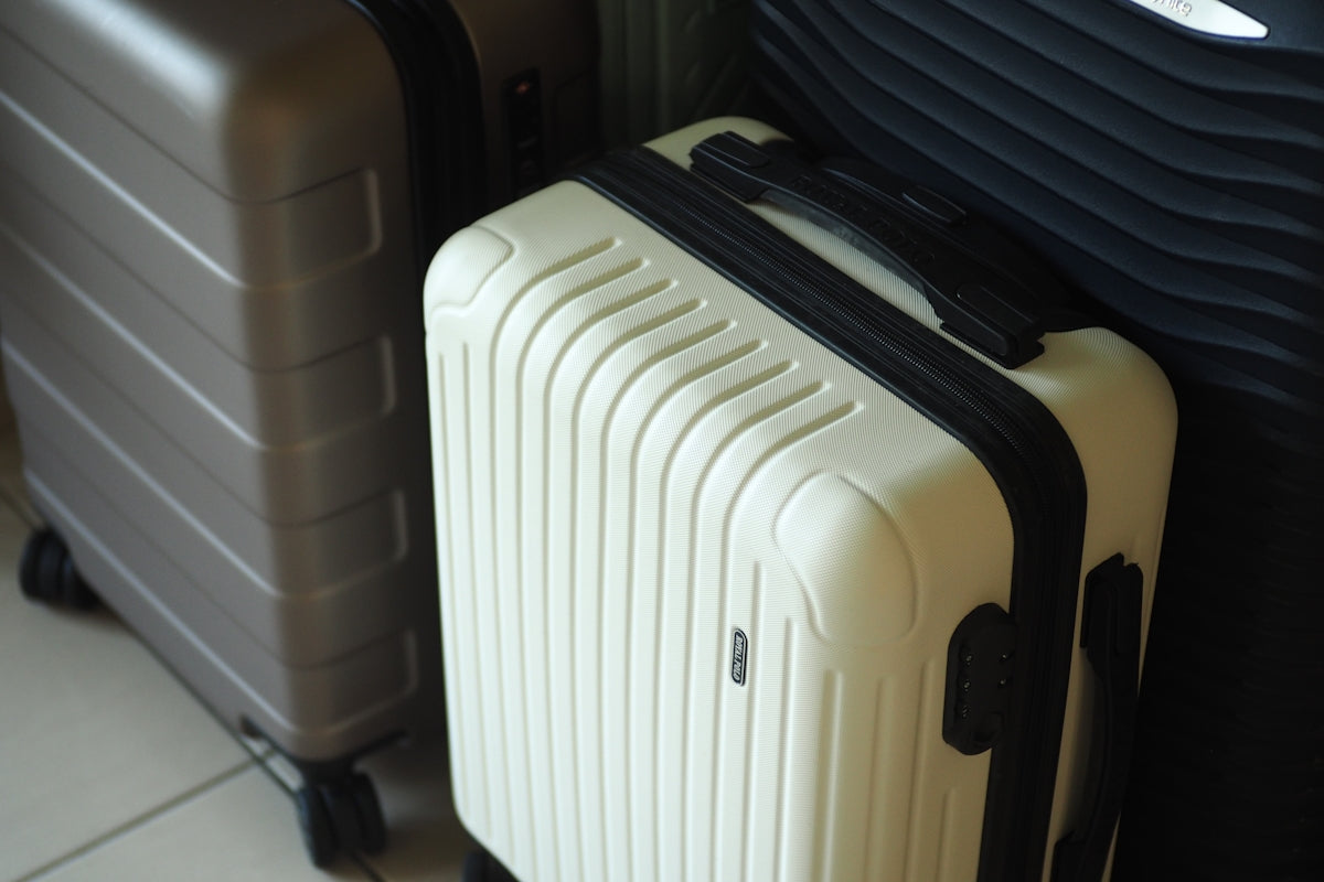 Three hard-shell suitcases in white, grey, and dark colors.