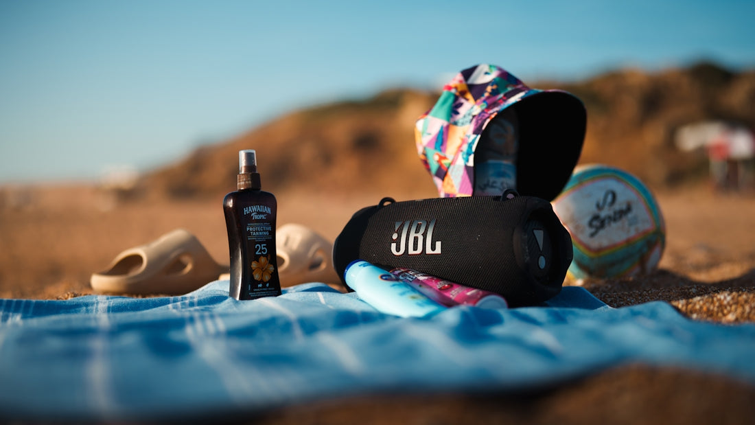 Beach essentials: jbl speaker, sunscreen, sandals, towel, and hat.