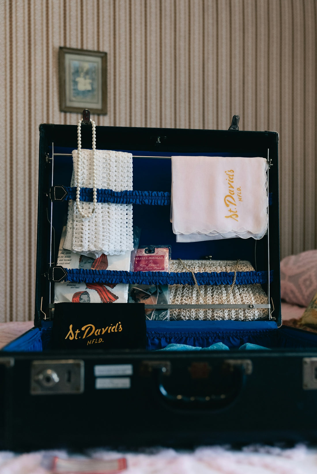 Vintage suitcase packed with pearl necklace, towel, and pink camera.
