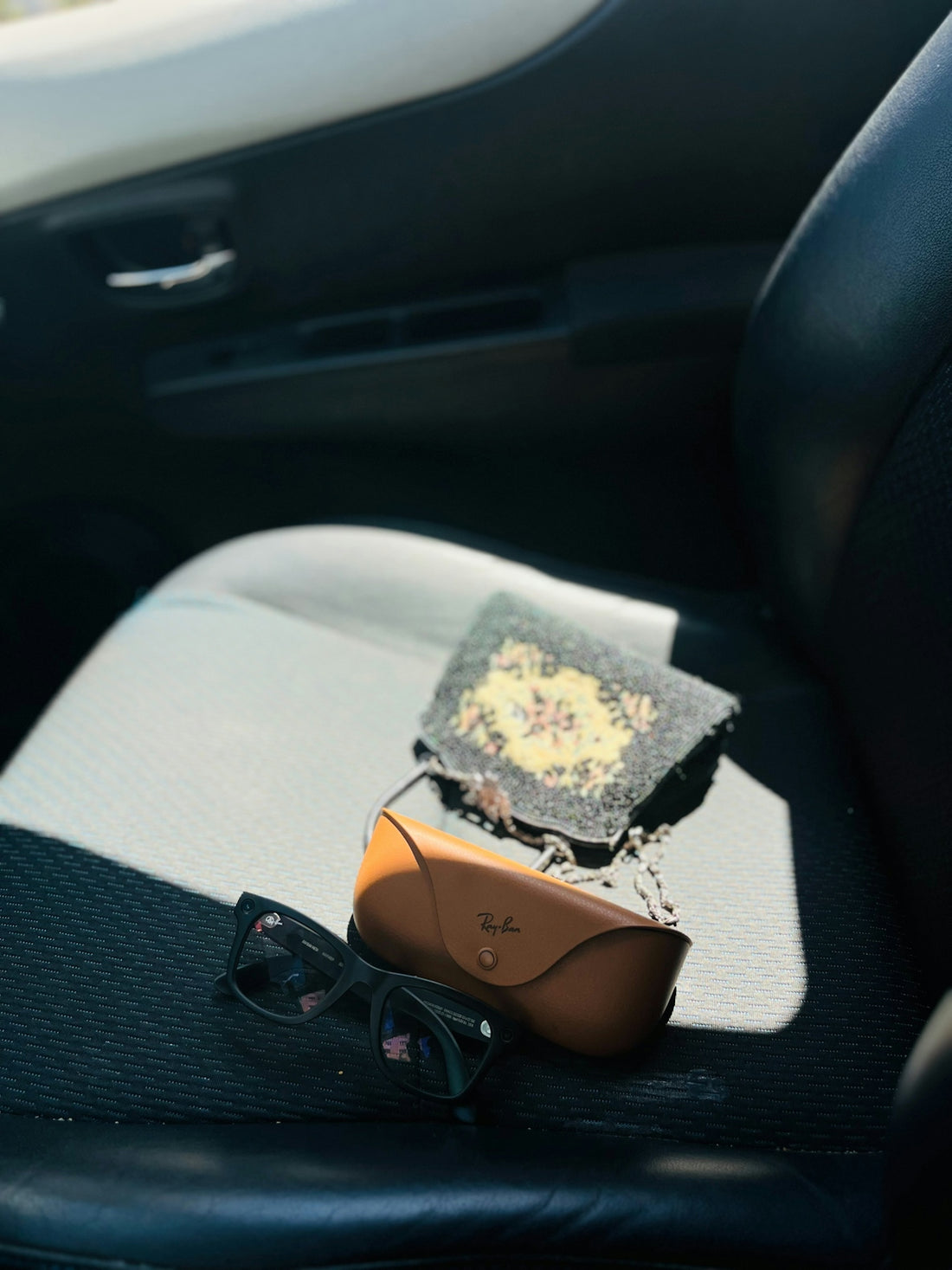 Sunglasses, case, and small patterned bag on a car seat
