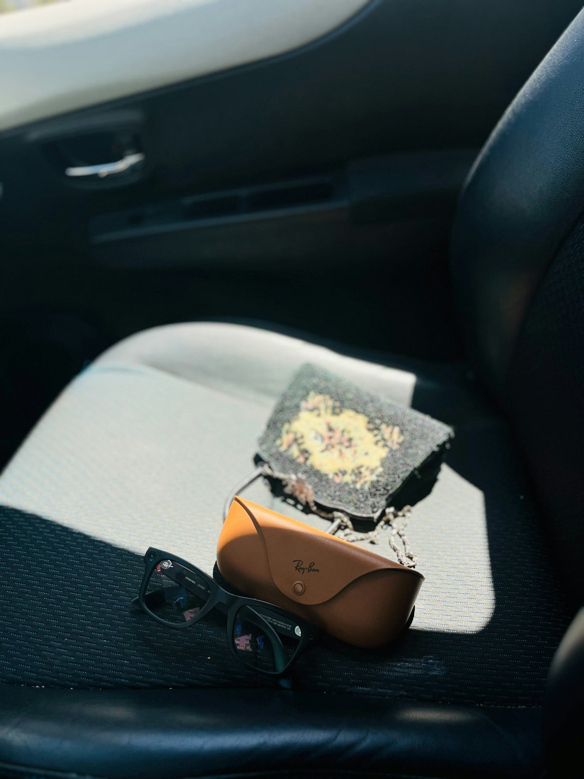 Sunglasses, case, and small patterned bag on a car seat