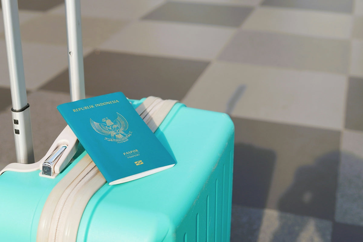An Indonesian passport resting on a bright turquoise suitcase at an airport